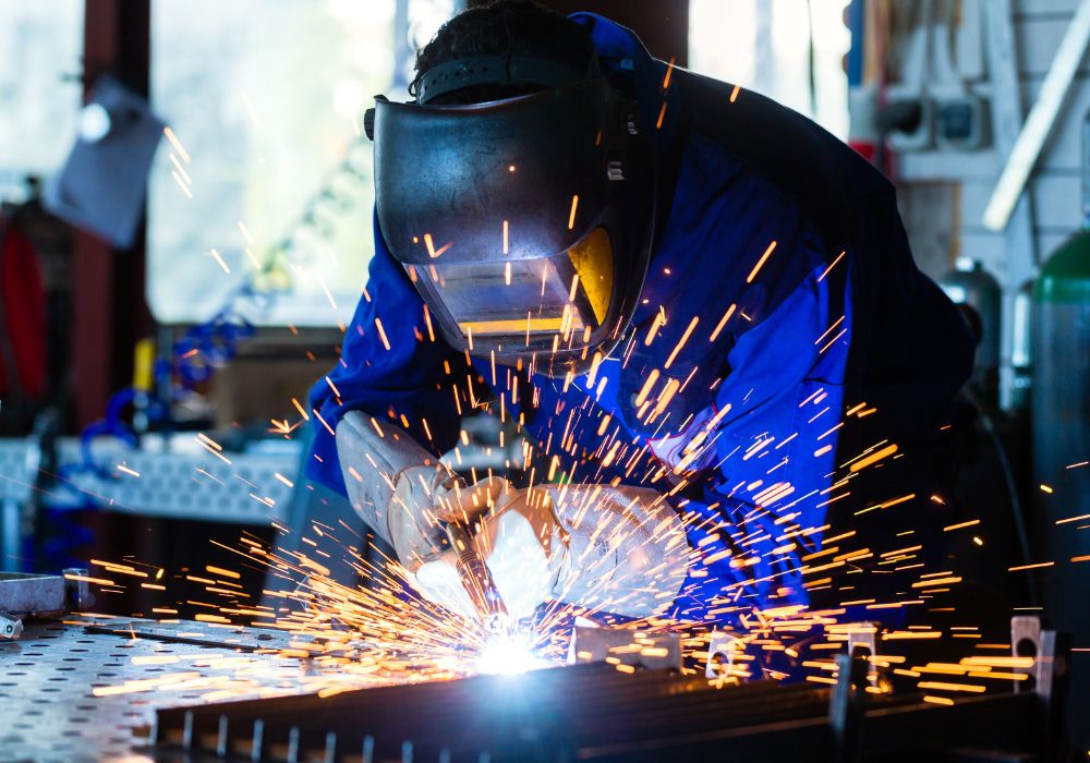 Certified welder performing precision welding with protective equipment in an industrial workshop